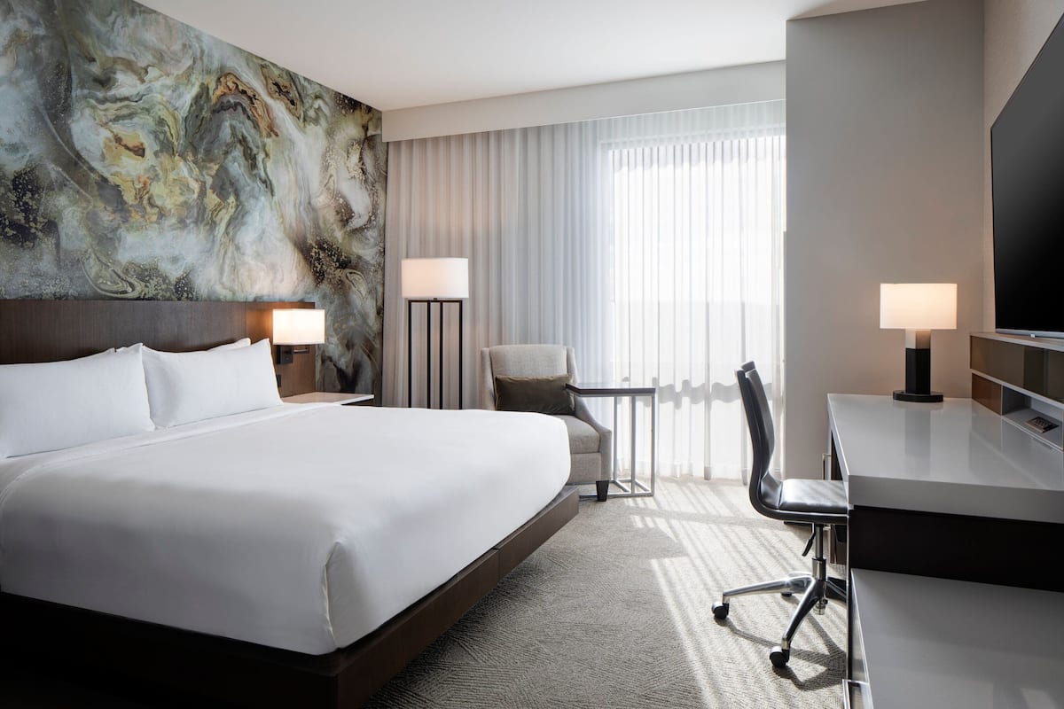 Une chambre d’hôtel avec un grand lit, un bureau, une chaise, deux lampes et un téléviseur.