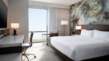 A hotel room with a large bed, a desk, a chair, a TV, and a view of the outdoors.