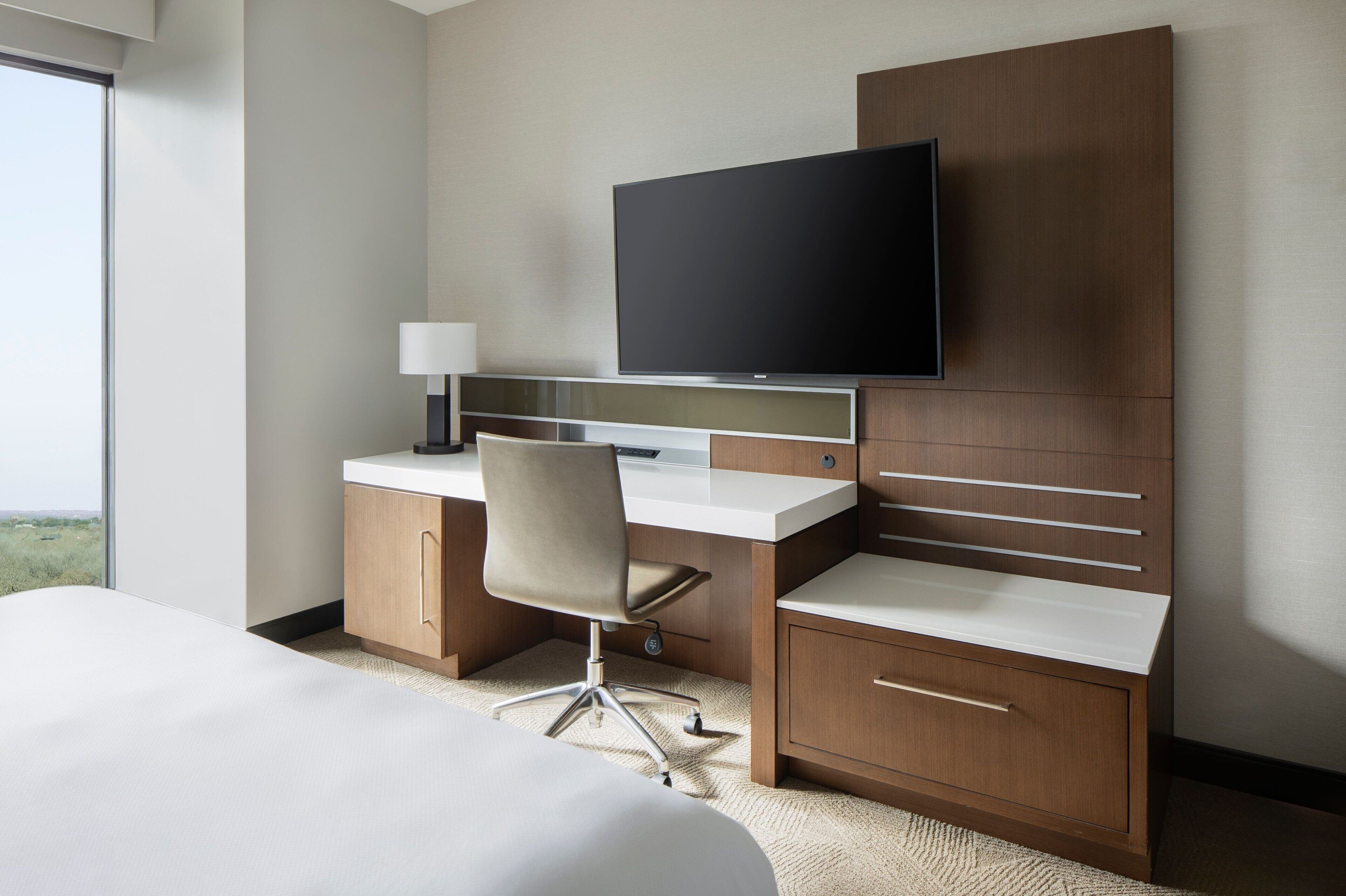 Una habitación de hotel con cama, escritorio, silla, televisión y armario.