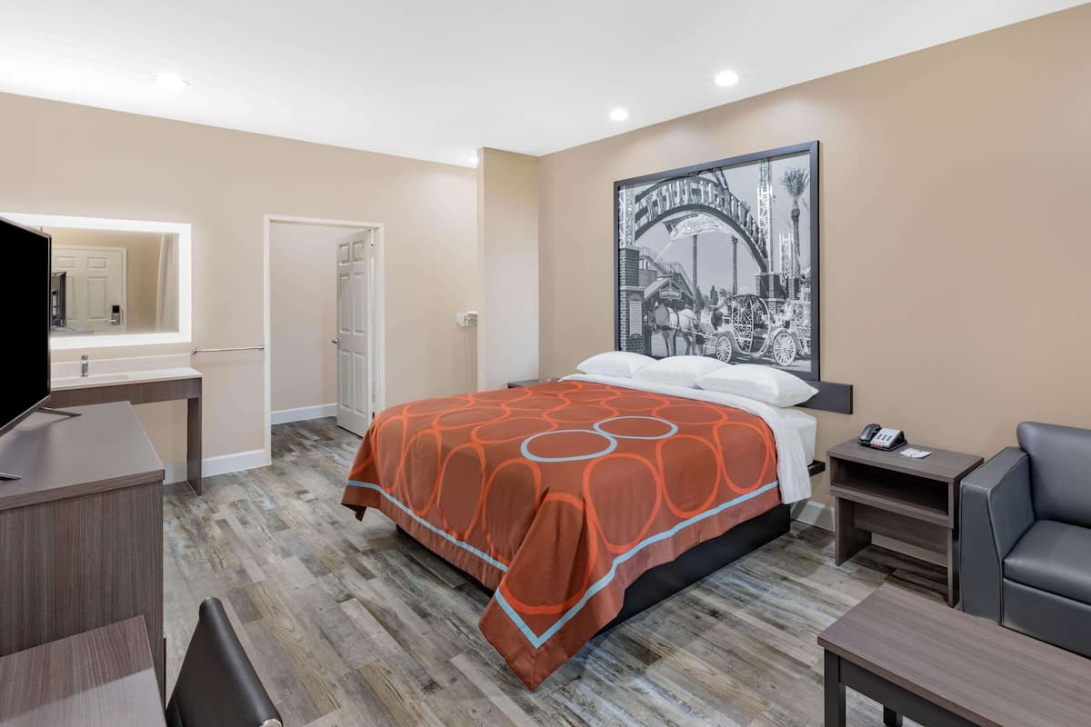 A hotel room with a bed, a desk, a chair, a nightstand, and a large framed picture on the wall.