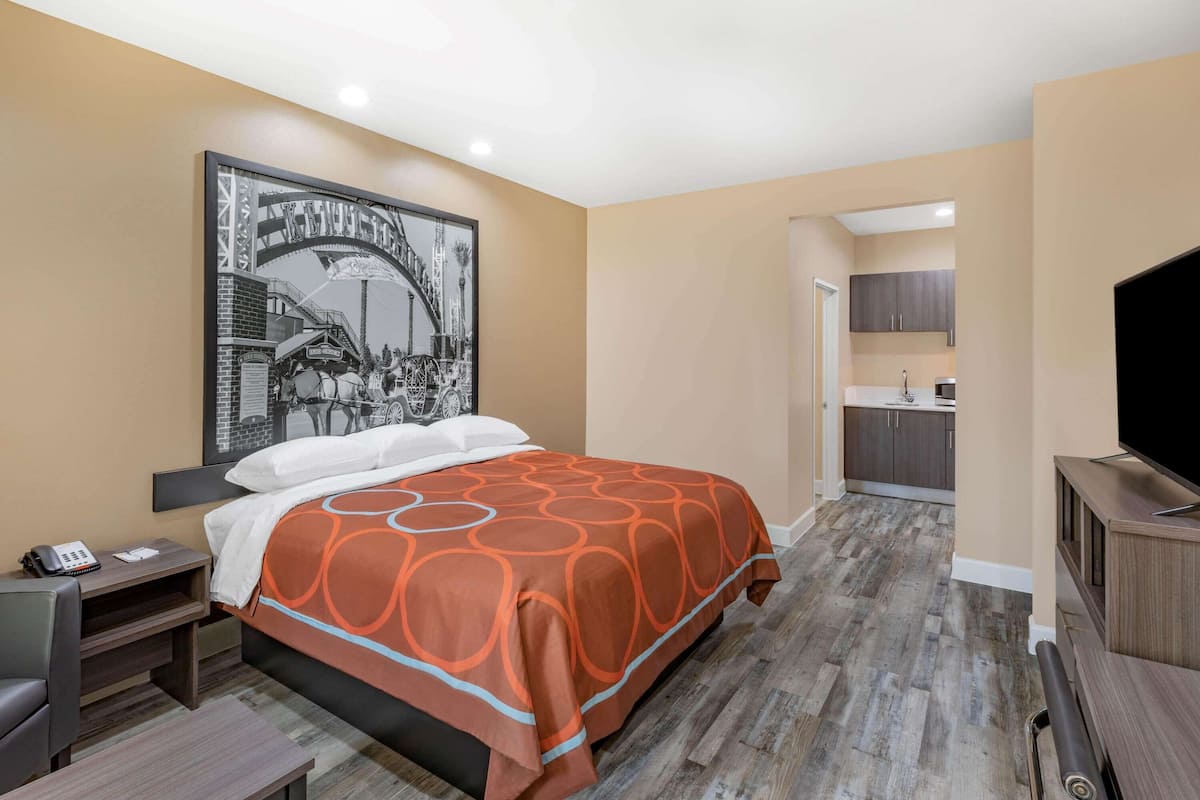 A hotel room with a bed, a desk, a chair, a television, and a kitchen area.