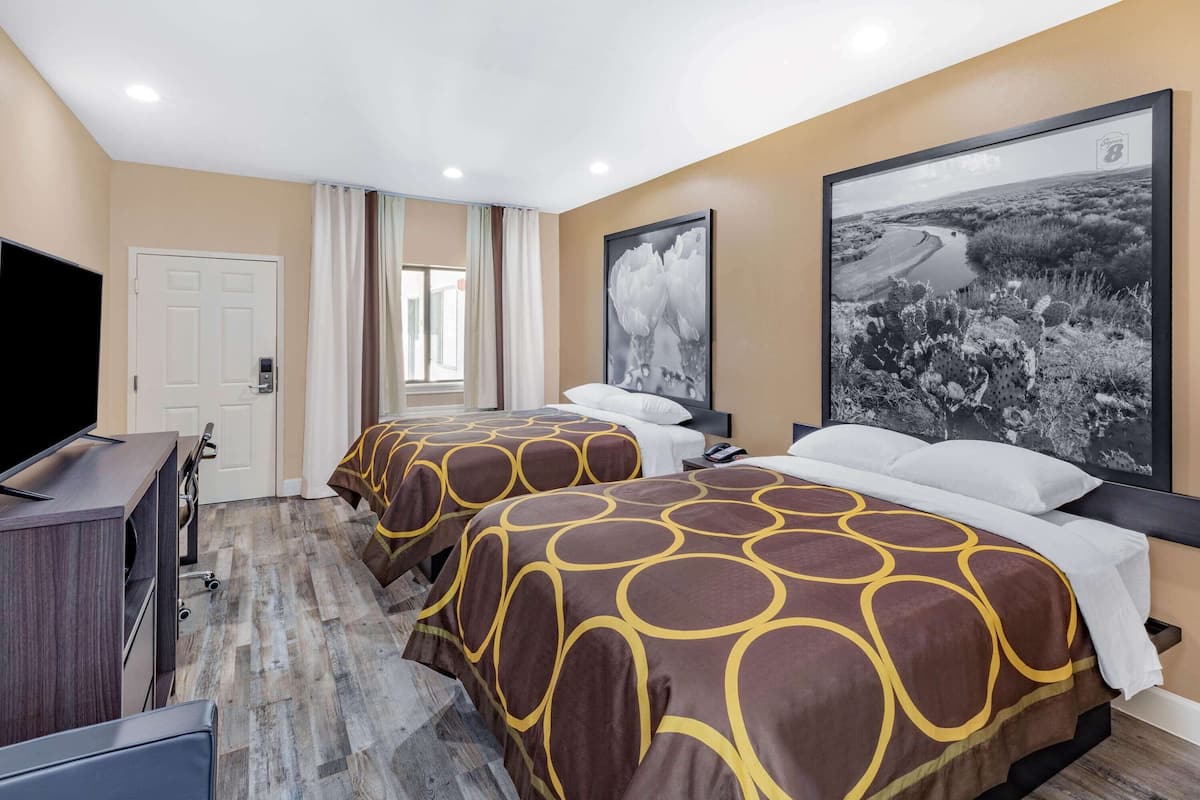 A hotel room with two beds, a TV, and a large landscape painting on the wall.