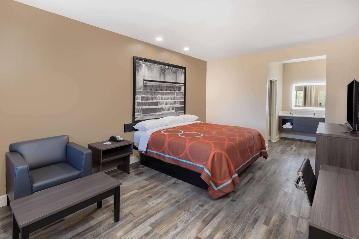 A hotel room with a bed, a chair, a desk, a nightstand, and a television.