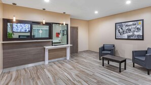 A reception area with a wooden reception desk, two grey chairs, a coffee table, and a framed 'Greetings Houston' sign. - Super 8 by Wyndham Houston NW Beltway 8/West Rd (Houston)