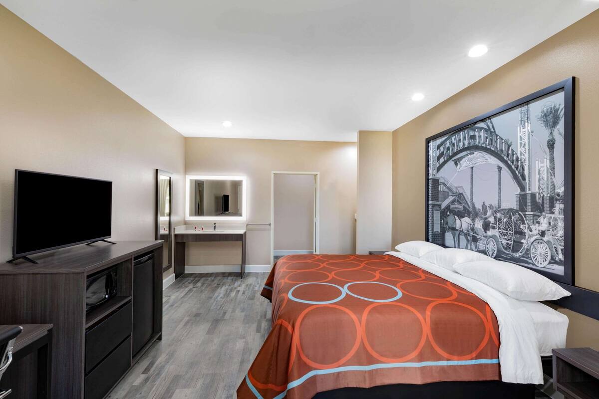 A hotel room with a bed, a TV, a desk with a mirror, and a large framed picture on the wall.