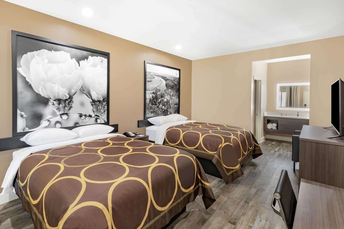 A hotel room with two beds, a large window, a desk, and a bathroom visible through an open door.