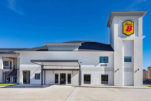 Un hotel moderno con techo plano, zona de estacionamiento cubierta y un llamativo letrero de 'Super 8 by Wyndham'.
