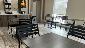 A modern café with wooden flooring, black chairs, and tables. There is a coffee machine and a fruit juice dispenser on the counter. - Super 8 by Wyndham Houston NW Beltway 8/West Rd (Houston)