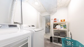 A laundry area with two washing machines, a drying rack, and shelves with folded towels and laundry supplies.