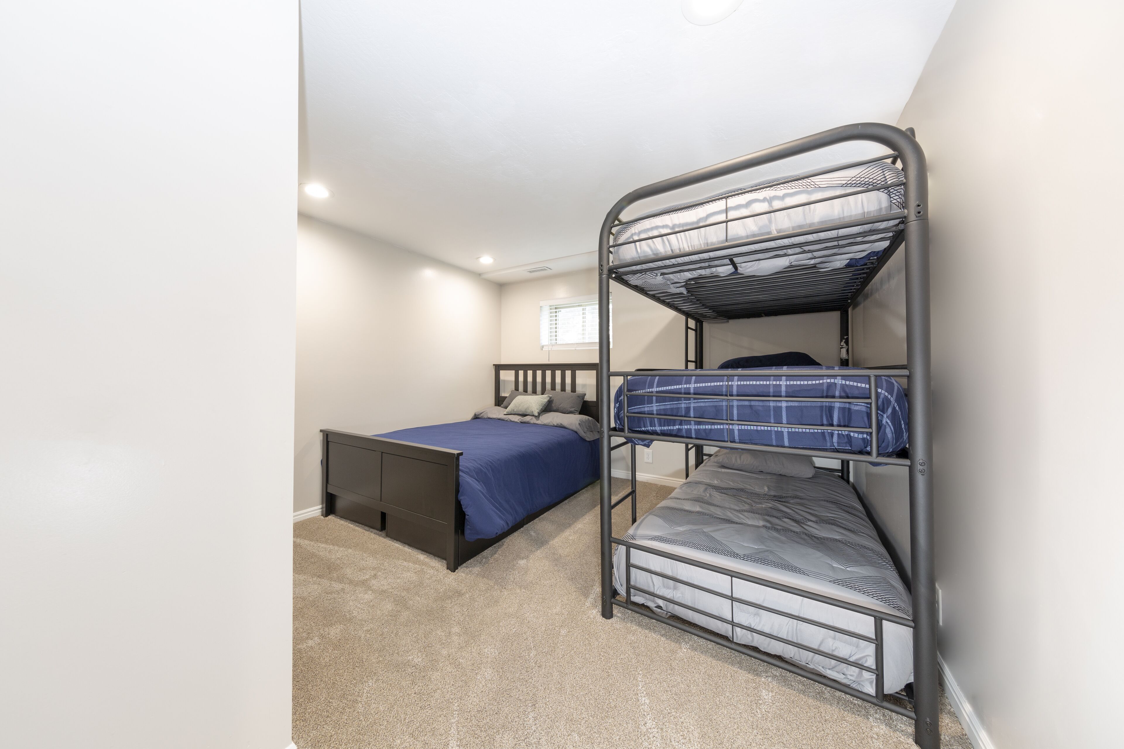 A bunk bed room with a single bed and a bunk bed, carpeted floor, and a window with blinds.