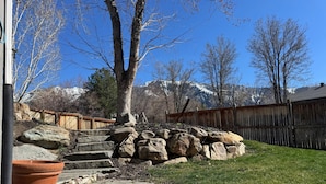 A stone pathway leading to a grassy area with a wooden fence and a tree.