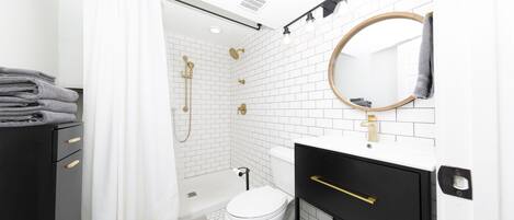 A modern bathroom with a white tiled shower, a toilet, and a vanity with a mirror.