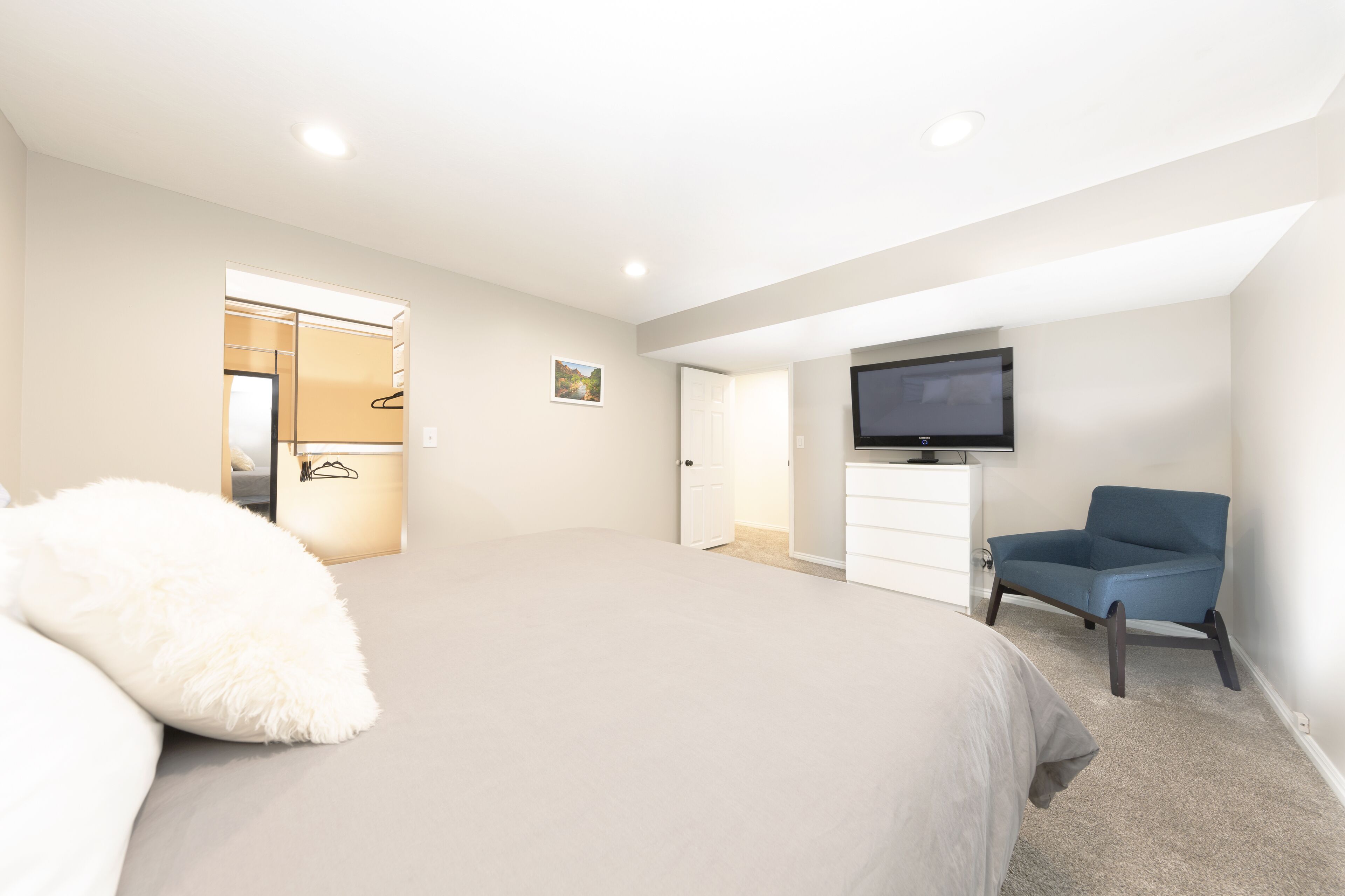 Un dormitorio con cama, una silla, televisor y armario.