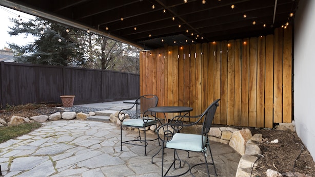 A patio with stone flooring, metal chairs, and a wooden fence.