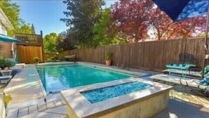 A rectangular swimming pool with a stone border, surrounded by a wooden fence and potted plants.