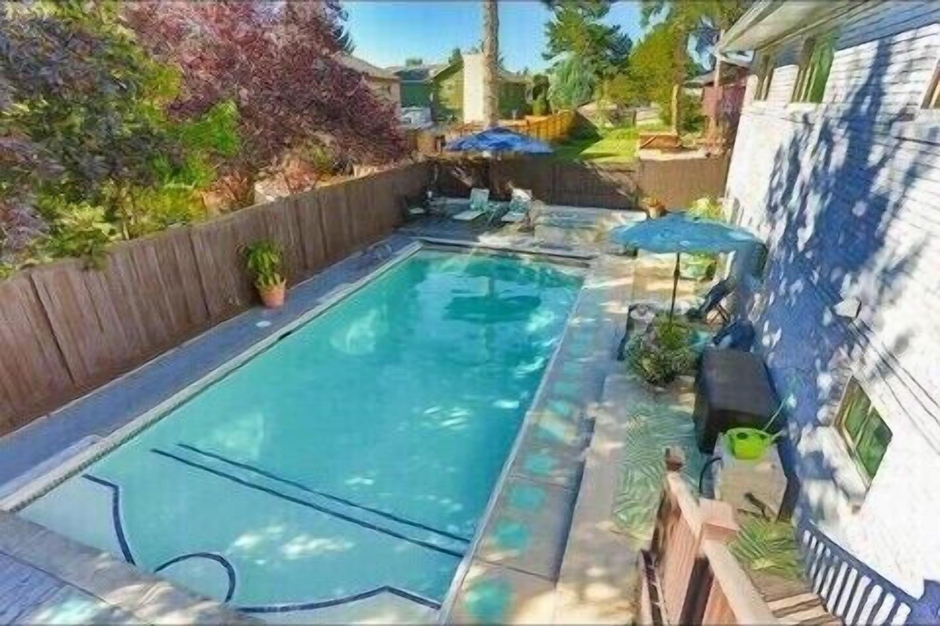 Una piscina rectangular con solárium de madera y un pequeño patio con mesa y sillas.