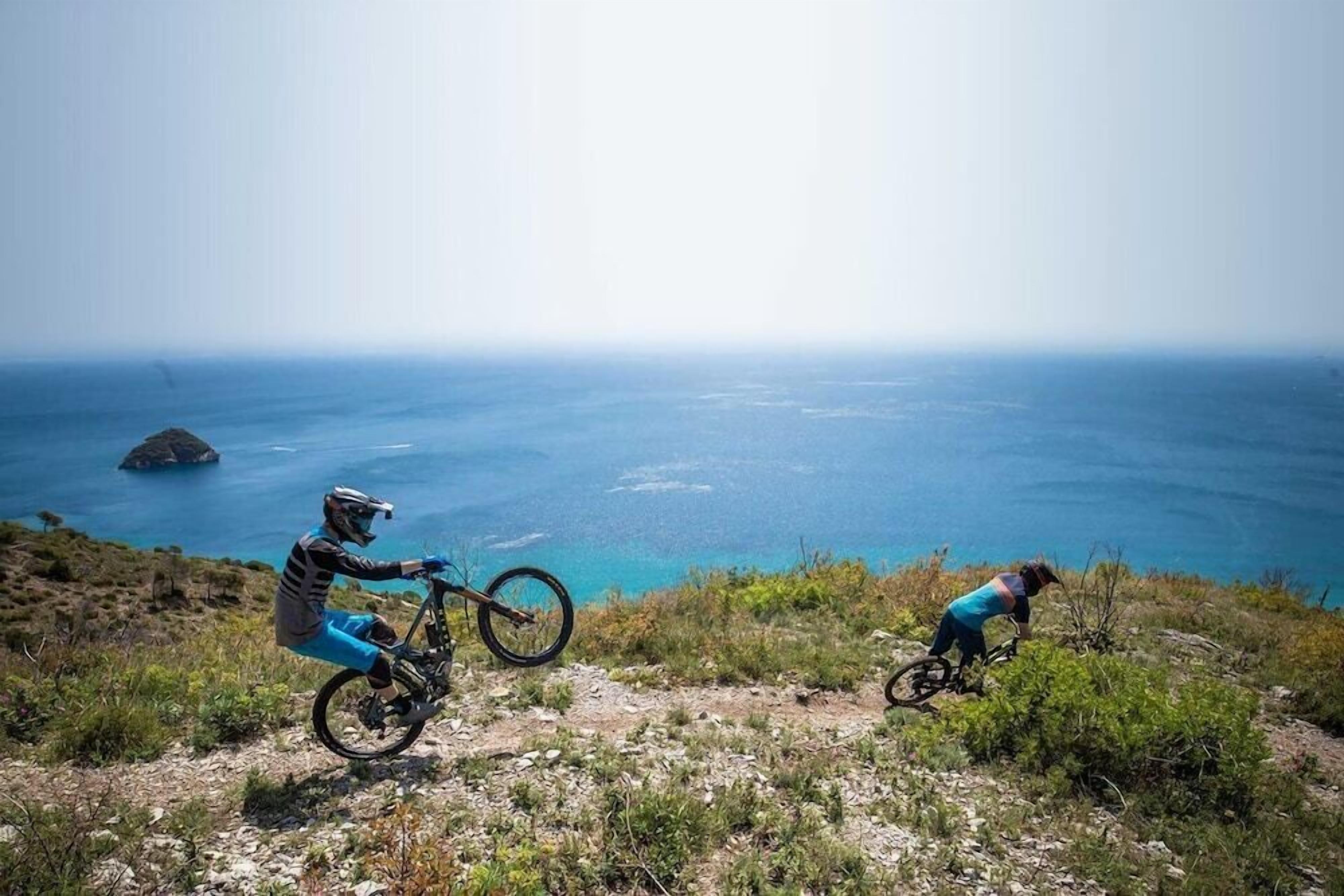 Two mountain bikers on a trail with a view of the ocean.