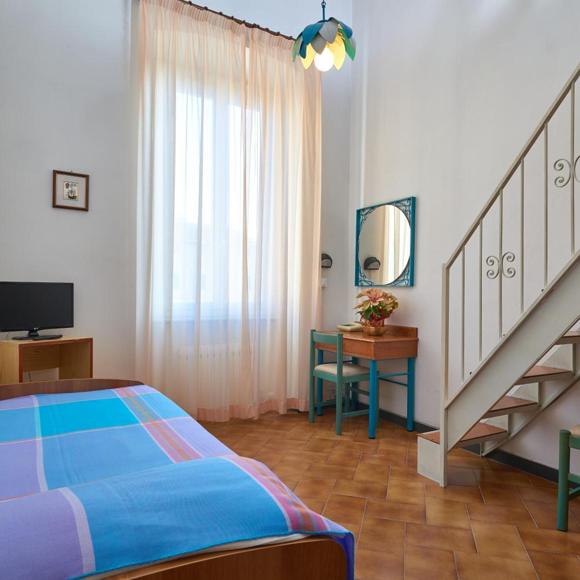 A bedroom with a bed, a desk, a chair, a television, a mirror, and a staircase.