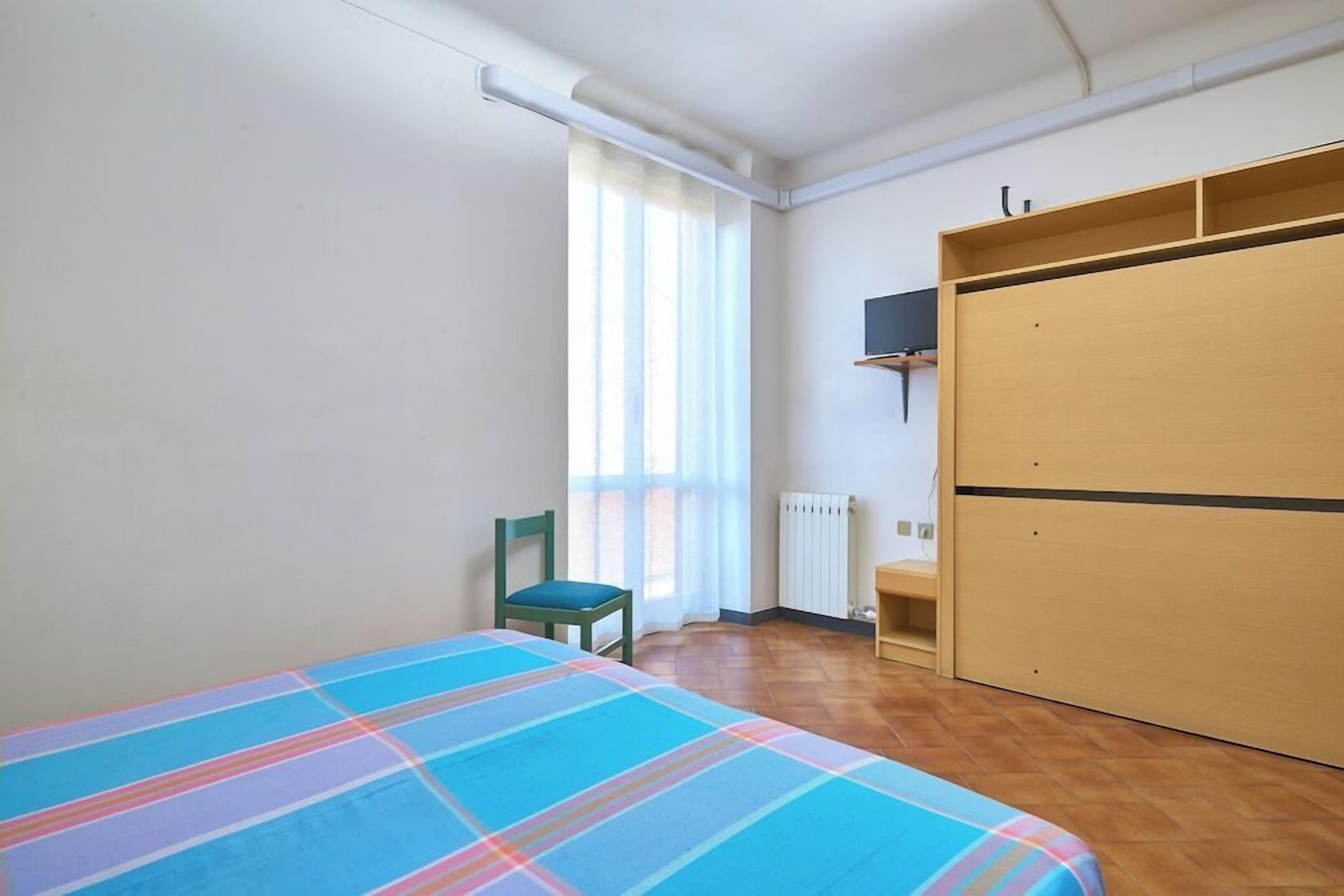 Een slaapkamer met een bed, een stoel, een kledingkast en een radiator.