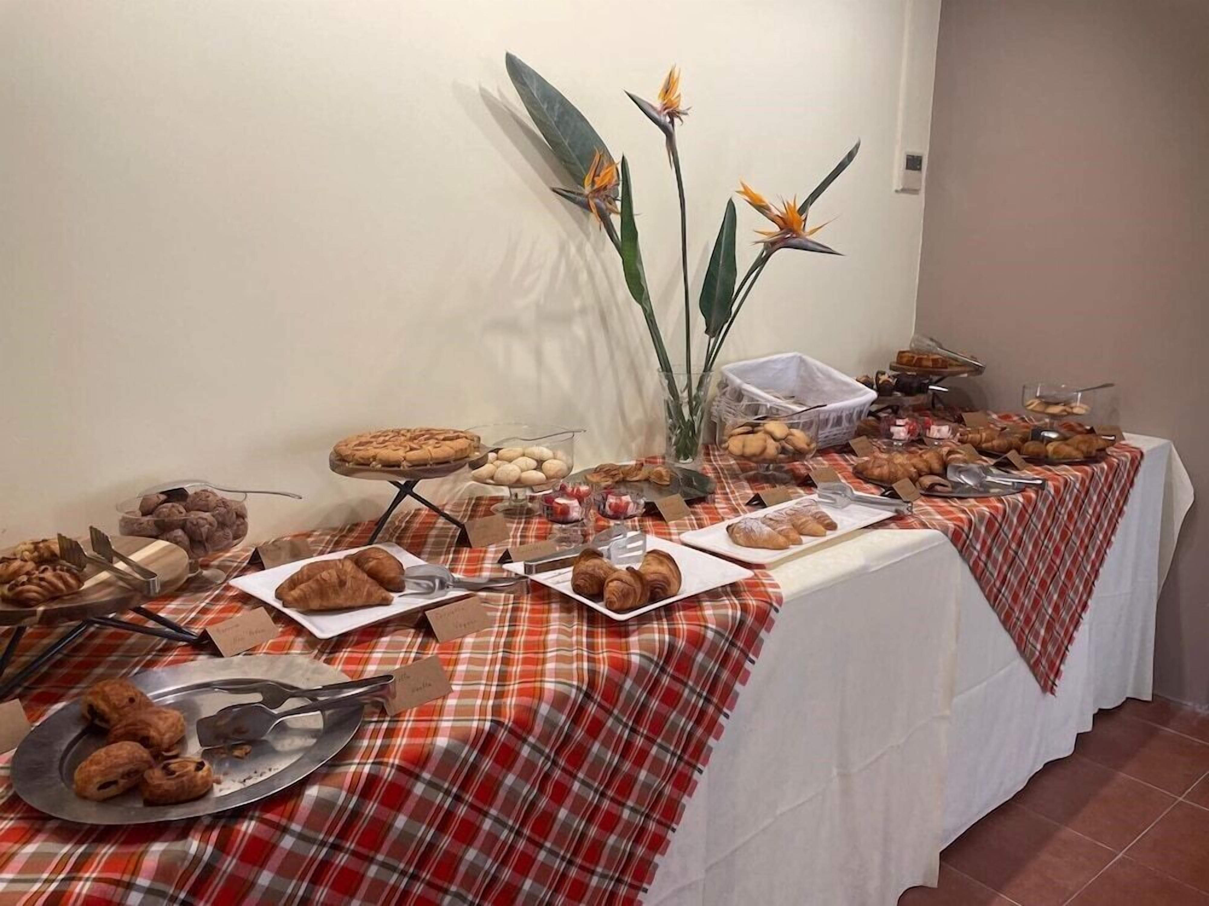 A buffet table with various pastries and desserts, including croissants and a pie, set on a red and white checkered tablecloth.