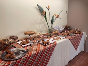 A buffet table with various pastries and desserts, including croissants and a pie, set on a red and white checkered tablecloth. - Hotel Garibaldi (Finale Ligure)