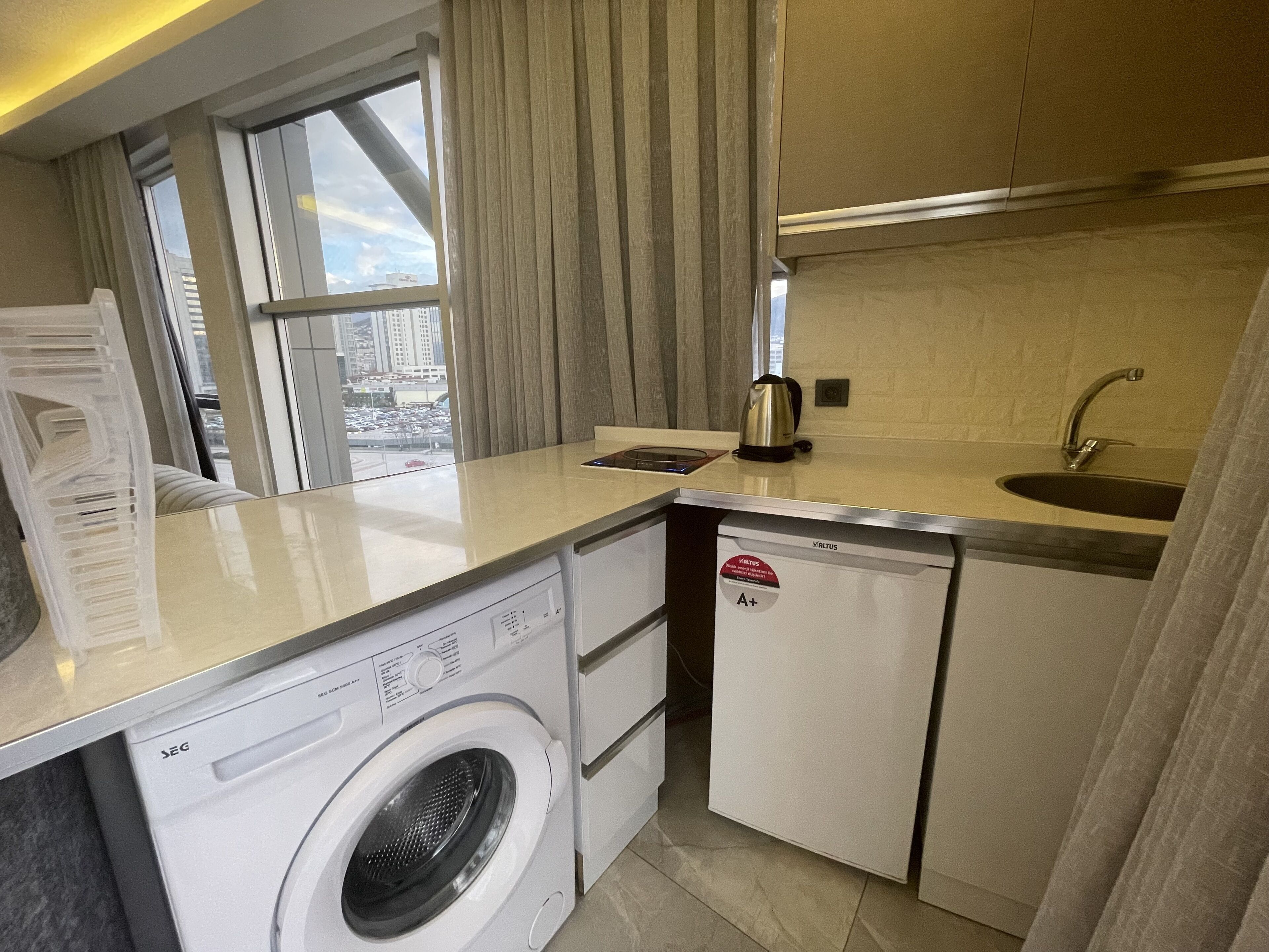 A compact kitchen with a washing machine, a kettle, and a sink.