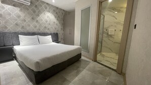 A modern bedroom with a large bed, a built-in bench, a walk-in closet, and a glass shower. - Le Luxe suites hotel & SPA (Bursa)