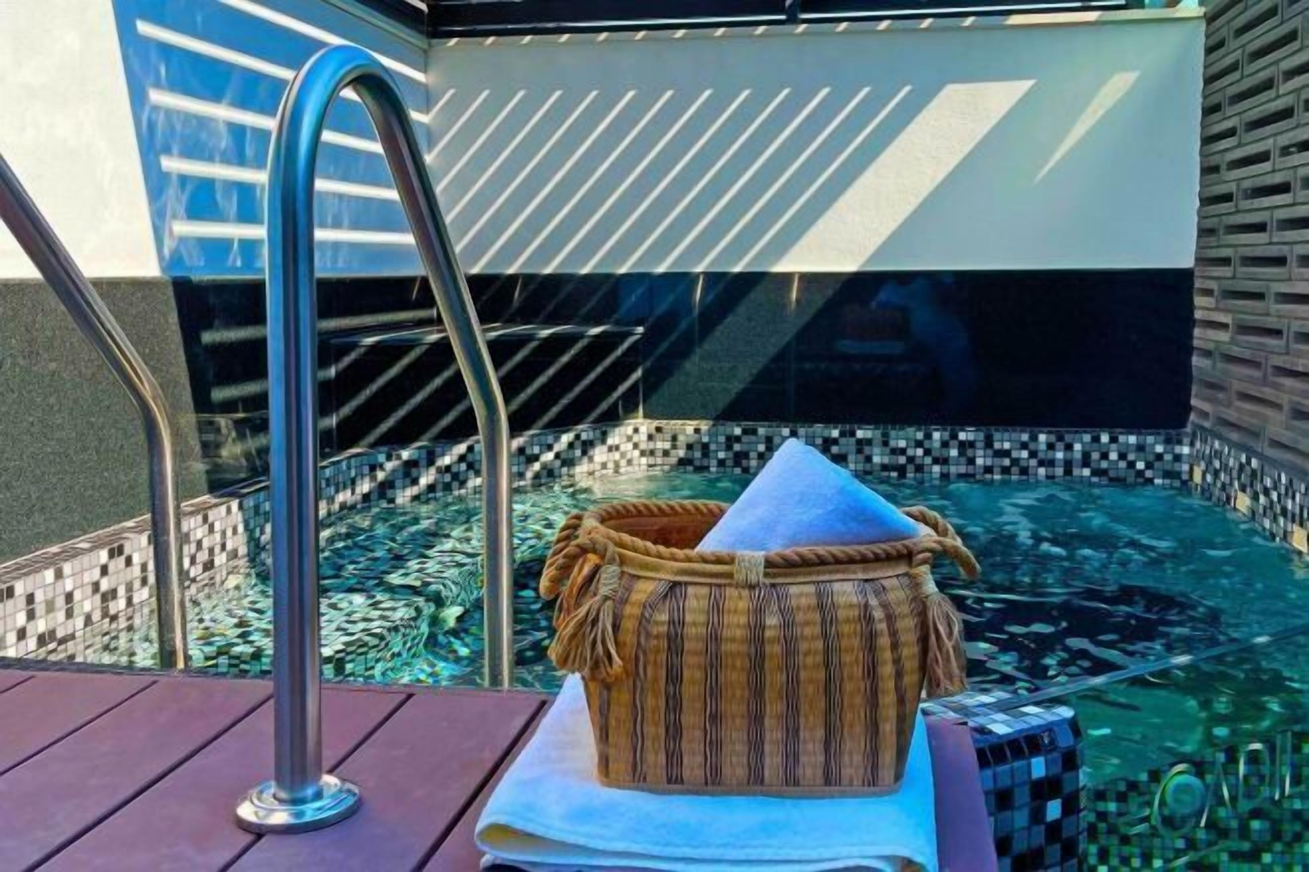 A pool area with a metal ladder, a woven basket, and a tiled wall.