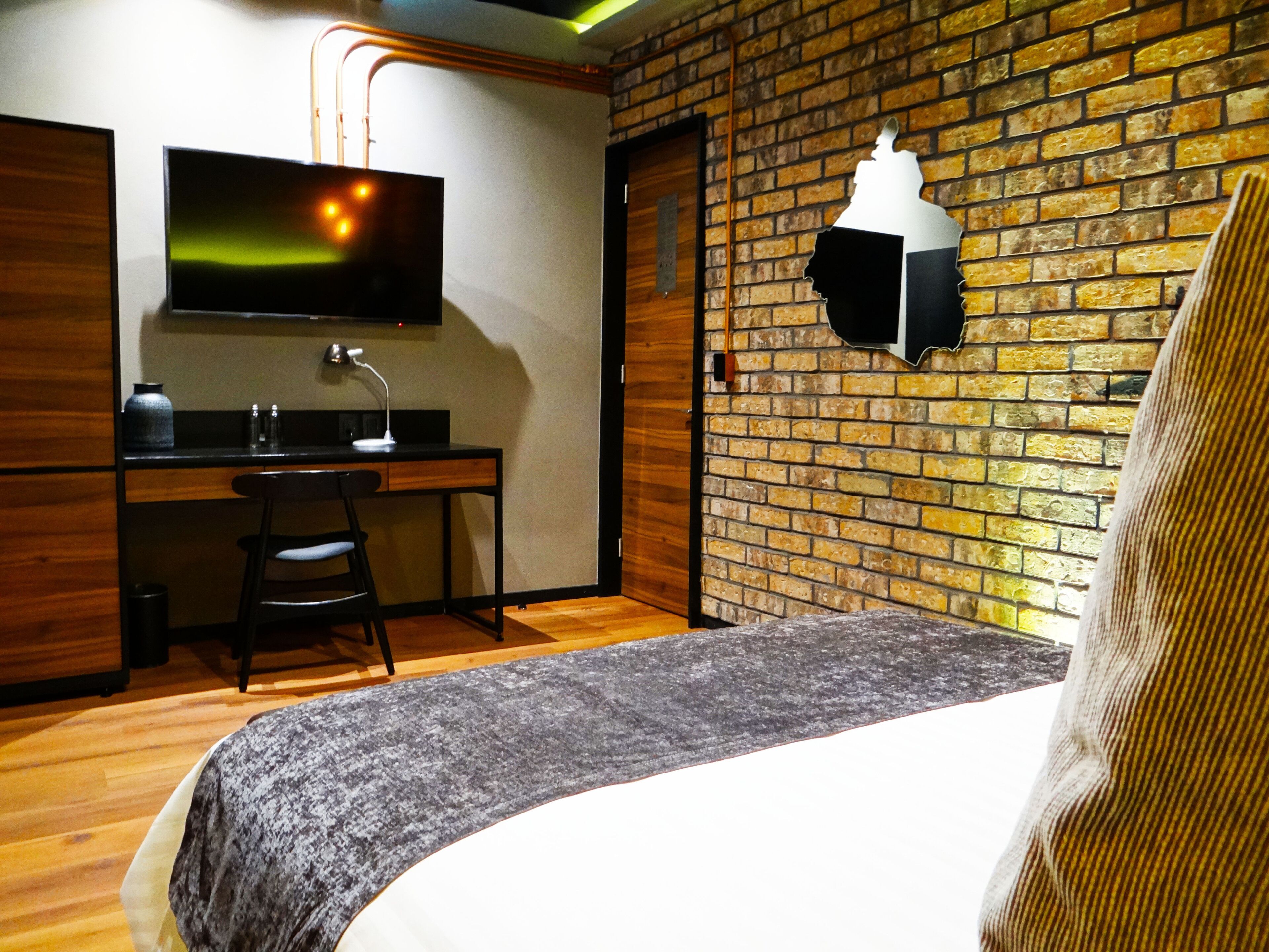 Una habitación de hotel con cama, escritorio, silla, televisión y pared de ladrillo.