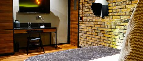 Una habitación de hotel con cama, escritorio, silla, televisión y pared de ladrillo.
