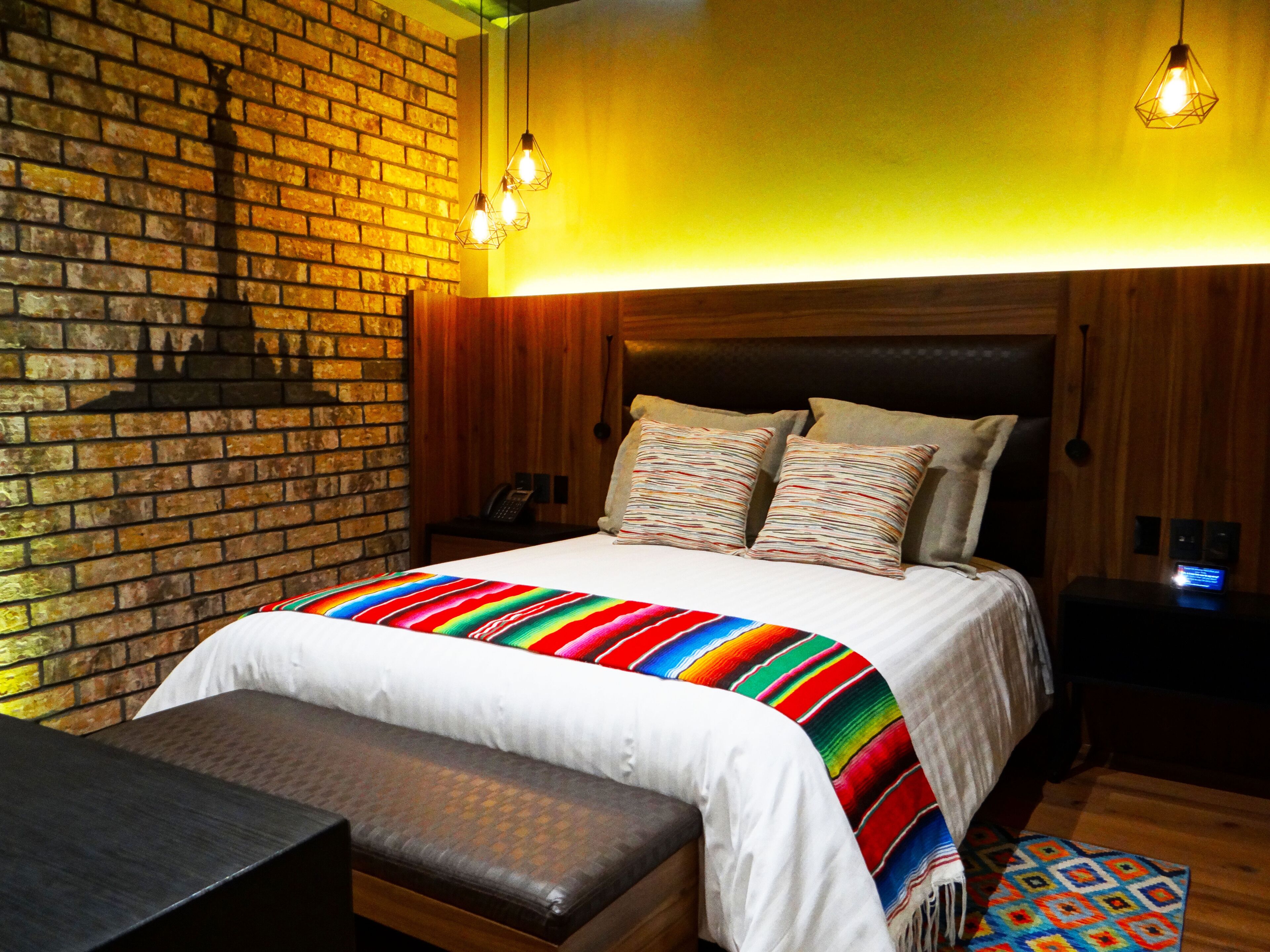Ein Hotelzimmer mit Backsteinwand, Holzkopfschild und einer farbenfrohen, gestreiften Bettdecke.