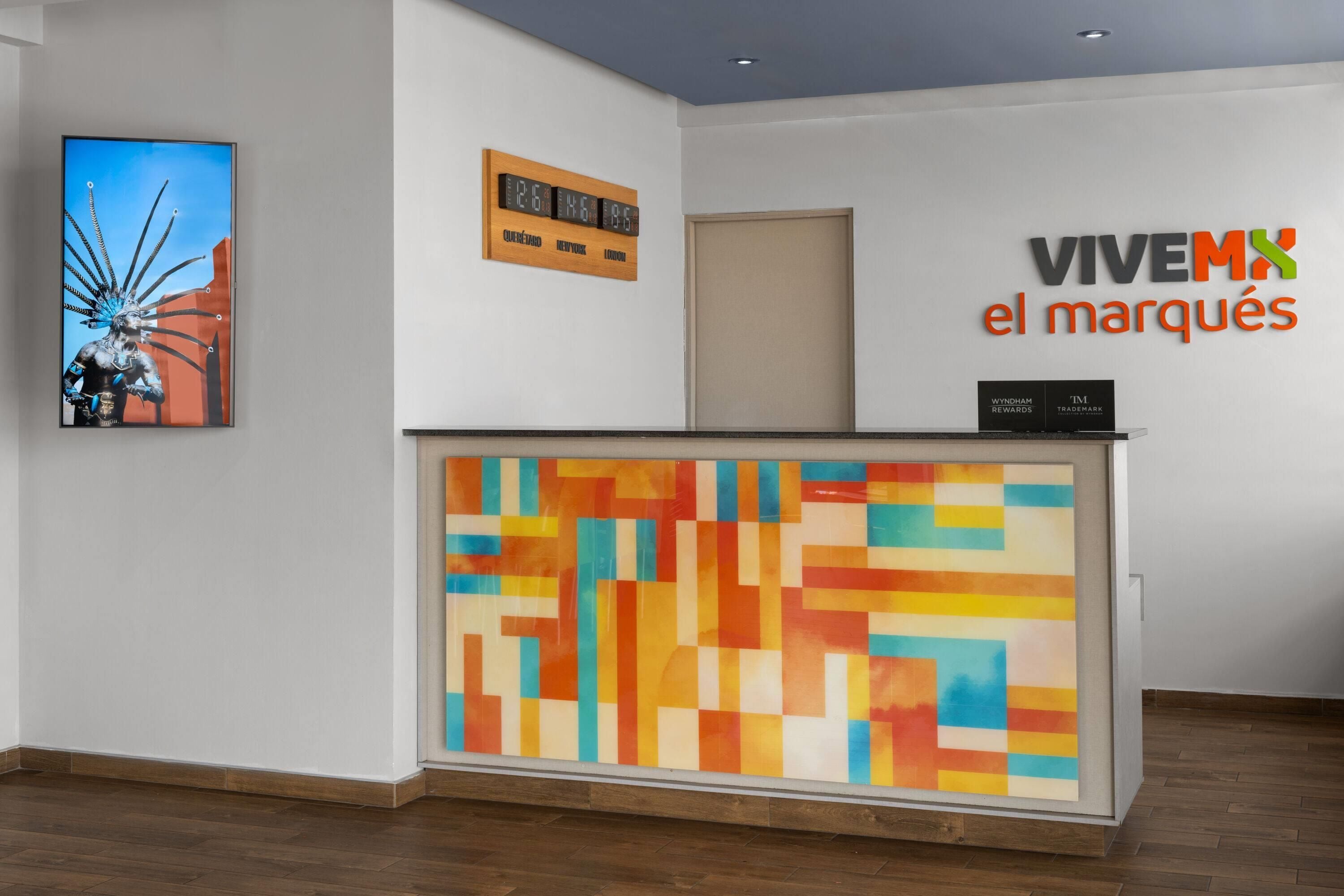 A reception desk with a colorful abstract artwork, a clock displaying time, and a sign with city names.
