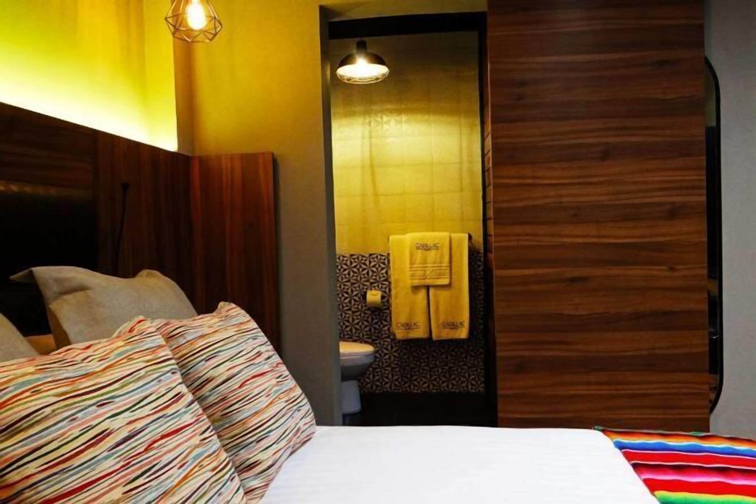 A bedroom with a bed, a wooden headboard, a bathroom with a toilet and a towel hanging on the wall.