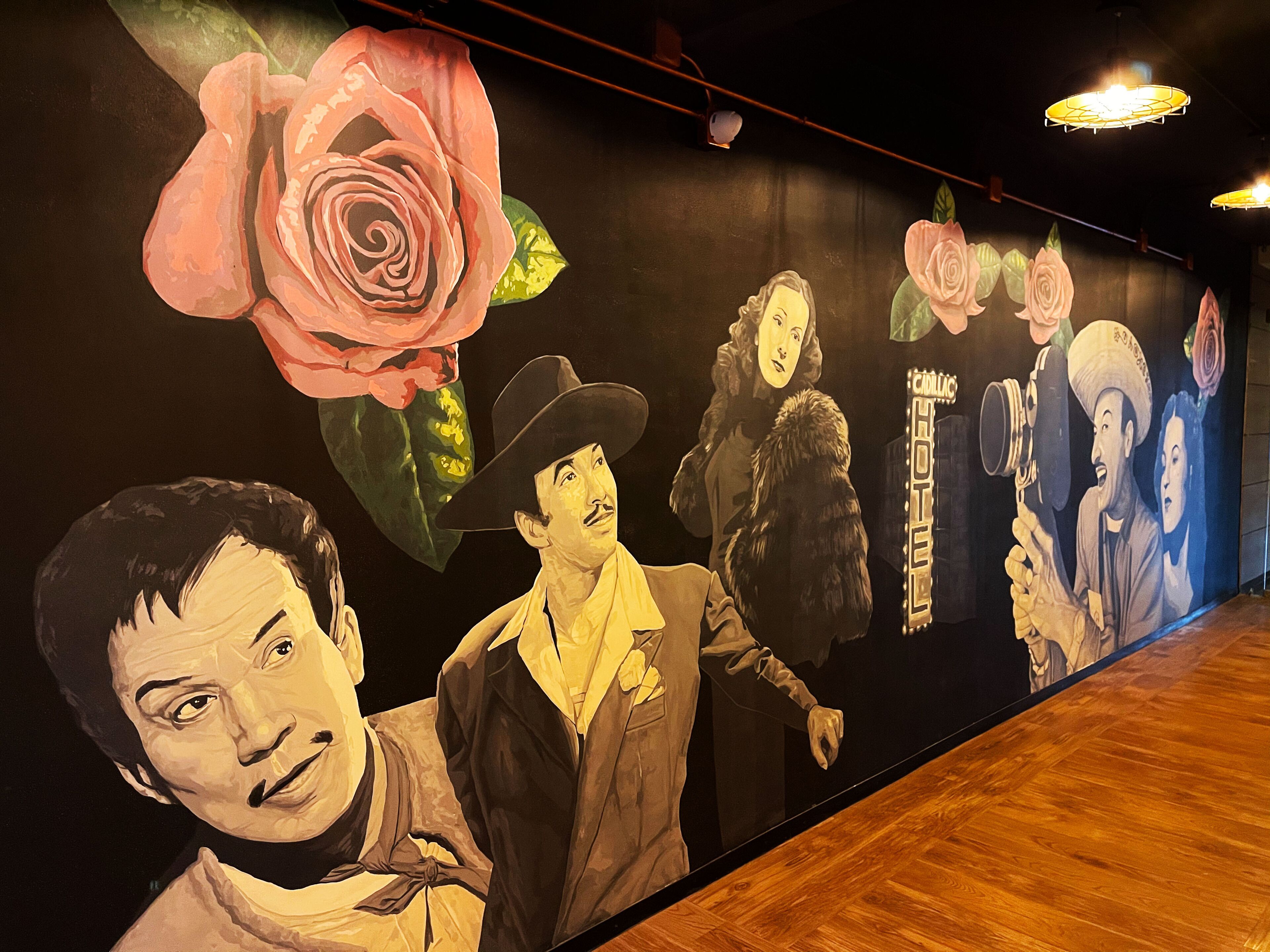 Un mural con rosas grandes y figuras de personas vestidas con ropas de época en una pared.