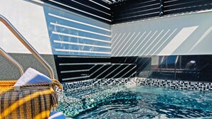 A modern indoor pool with mosaic tiles, a lounge area with a patterned chair, and a view of the outside. - Cadillac Hotel Boutique (Mexico City)