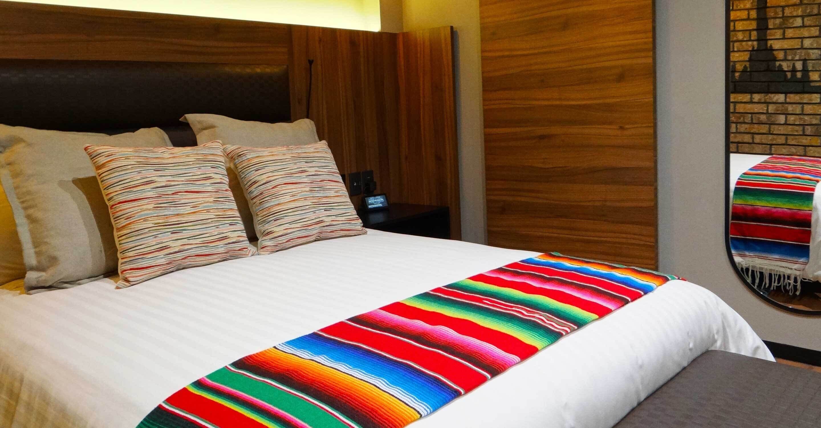 Quarto de hotel com uma cama grande, cabeceira de madeira e manta listrada colorida.