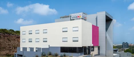 Un edificio moderno con fachada plana, múltiples ventanas y una llamativa pared rosa.