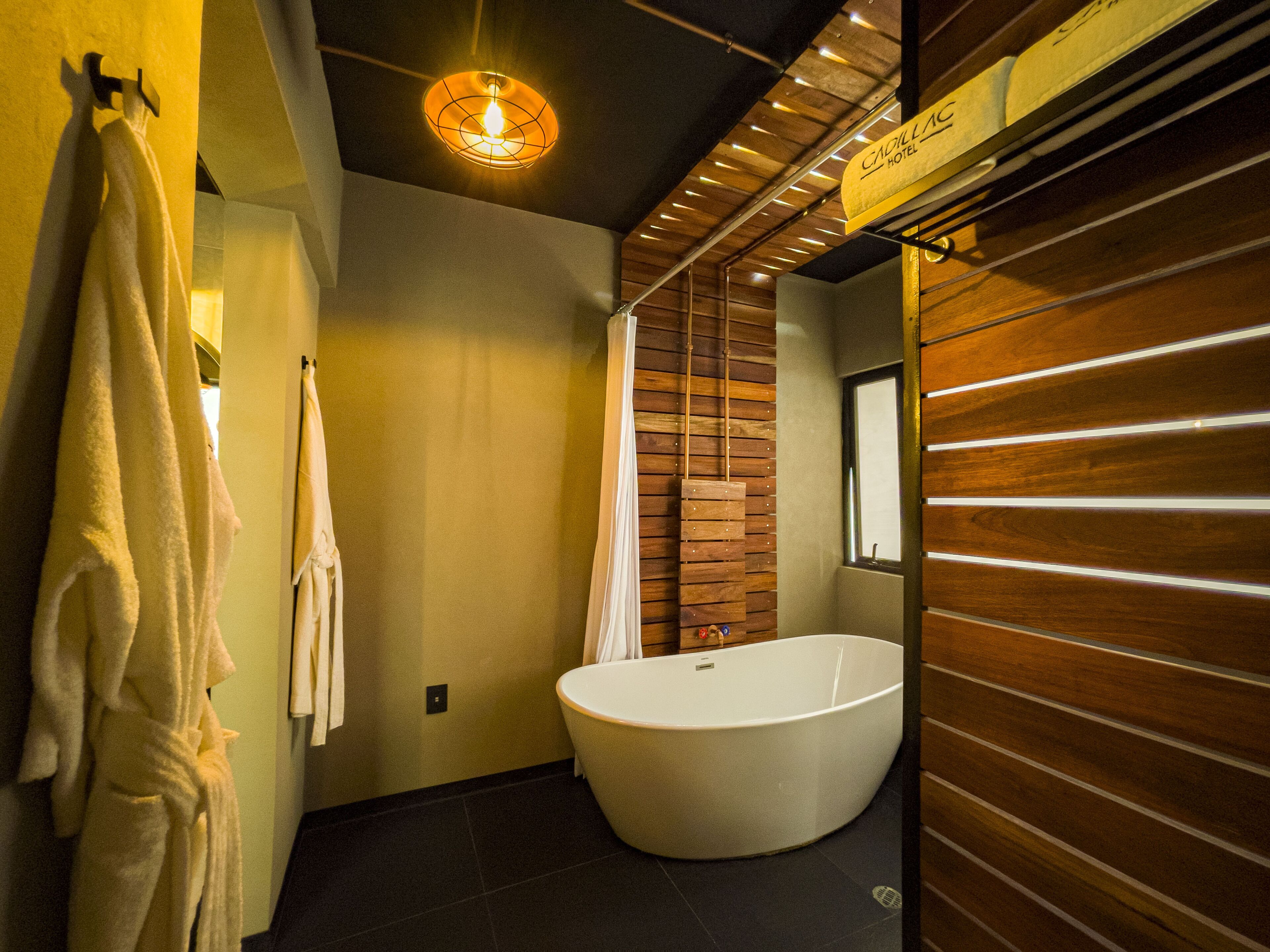 Un baño moderno con una bañera independiente, paneles de madera y un cartel que indica la ubicación como el Hotel Cadillac.