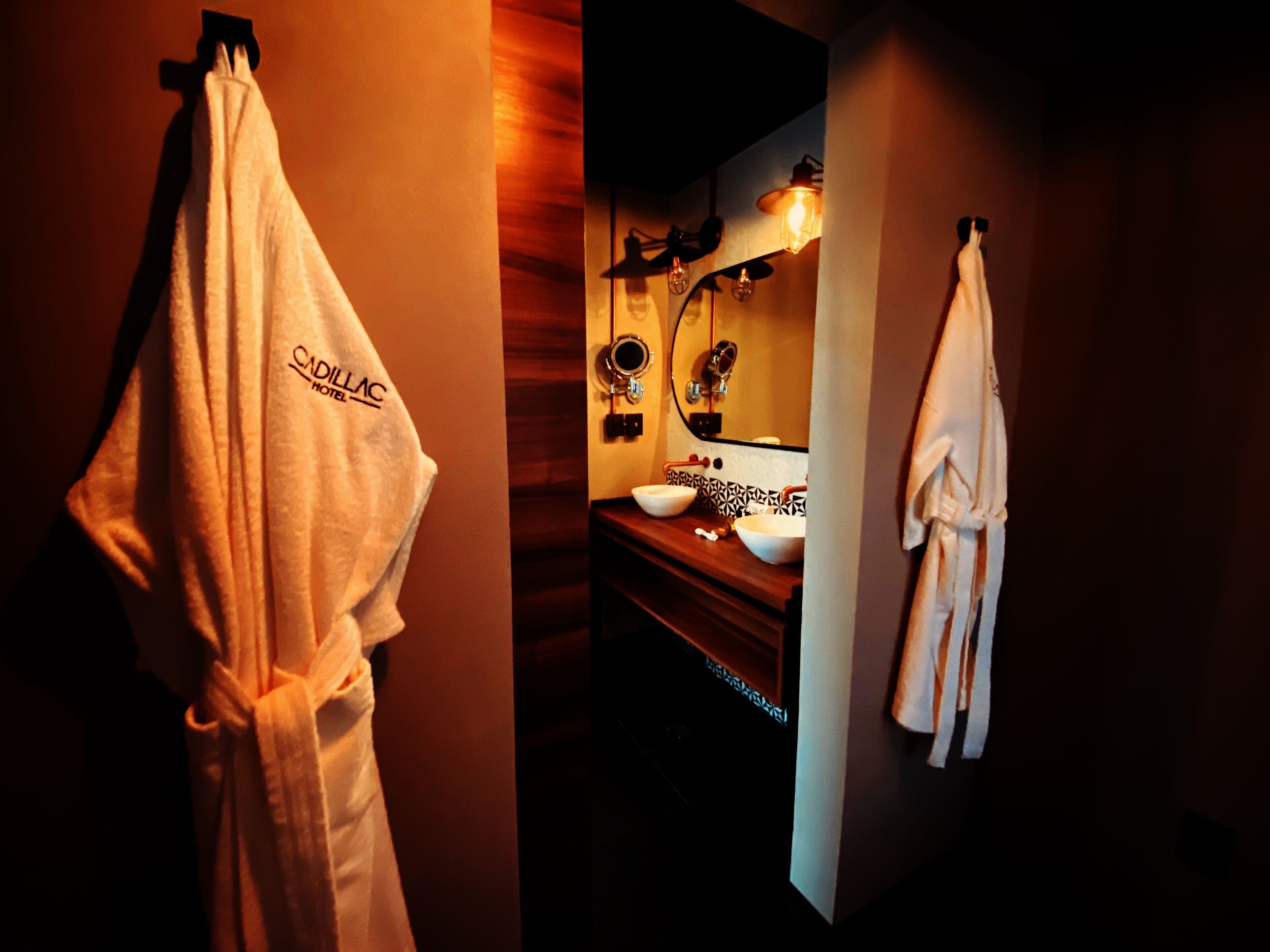 A hotel bathroom with a wooden vanity, two sinks, a mirror, and towels hanging on the wall.