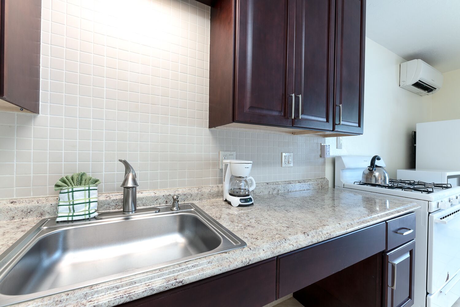 A kitchen with a stainless steel sink, a coffee maker, and a kettle on the countertop.