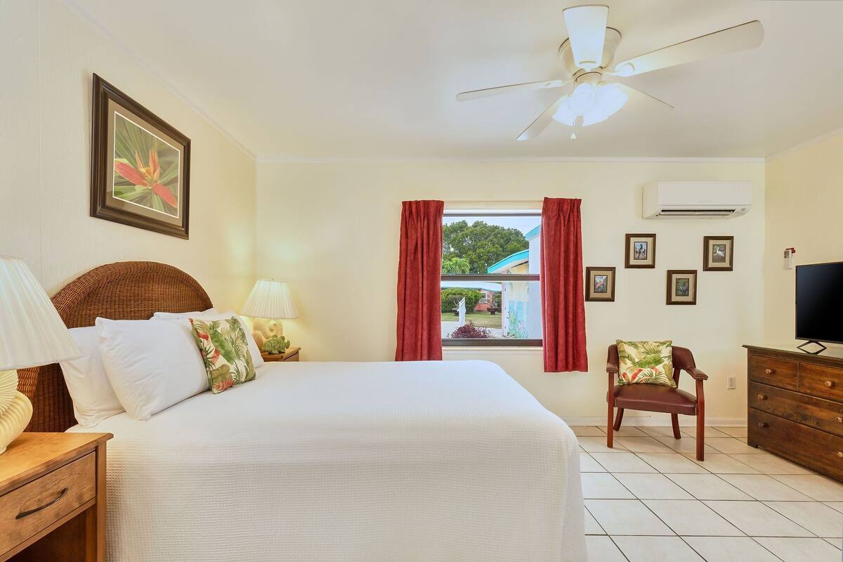 A bedroom with a bed, a chair, a dresser, a TV, and a window with curtains.