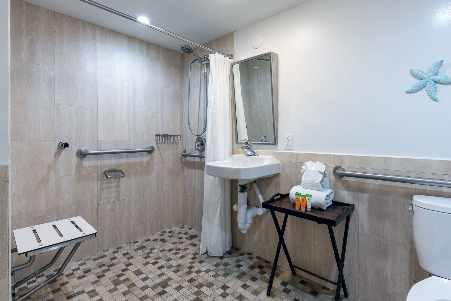 A bathroom with a shower, a sink, a toilet, and a small table with toiletries.