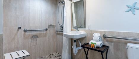 A bathroom with a shower, a sink, a toilet, and a small table with toiletries.