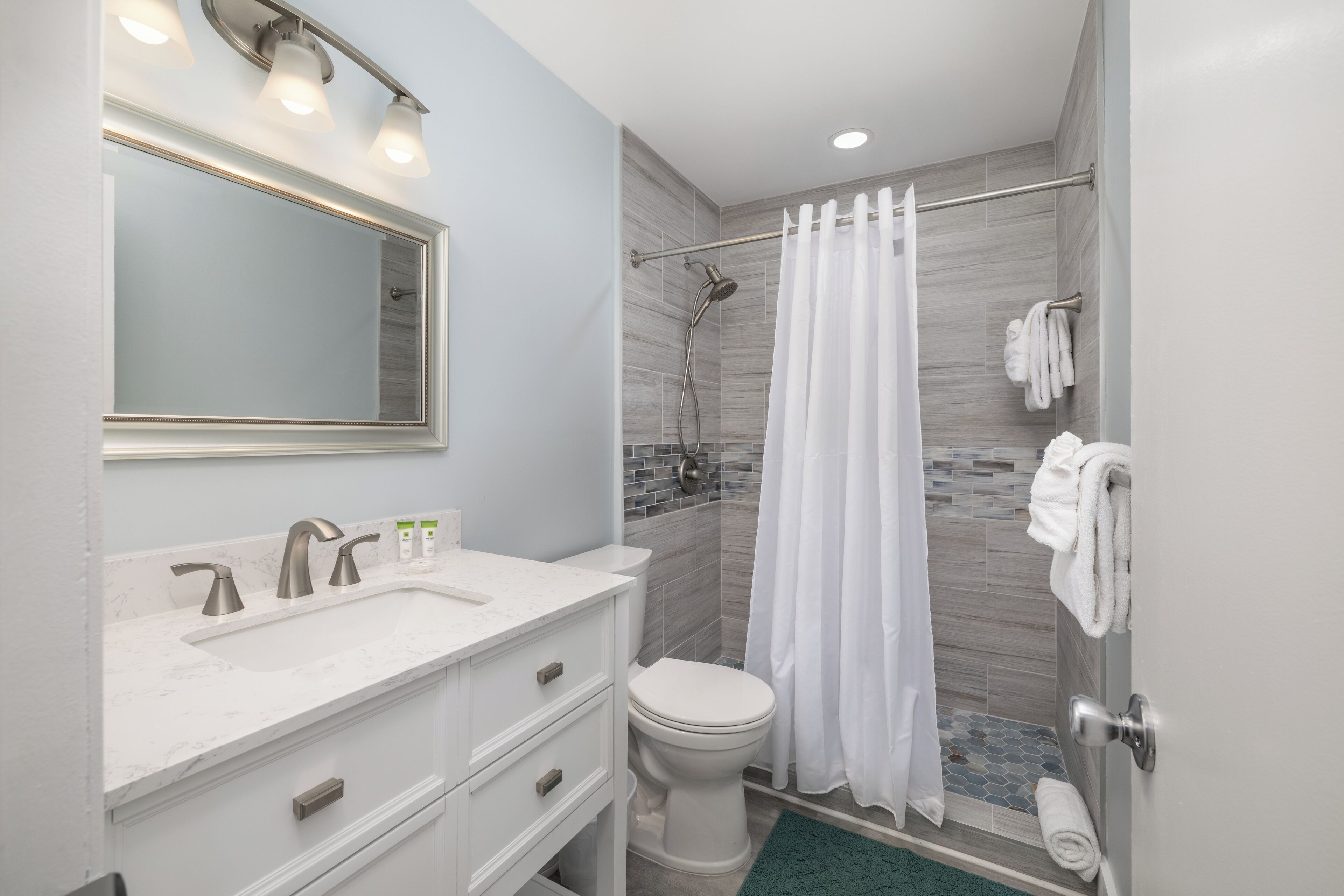 A modern bathroom with a white sink, mirror, and toilet, a shower with a glass door, and a towel rack with towels.