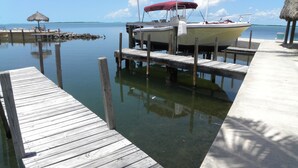 A wooden dock with a boat docked at the pier, a thatched umbrella, and calm water. - Rock Reef Resort (Key Largo)