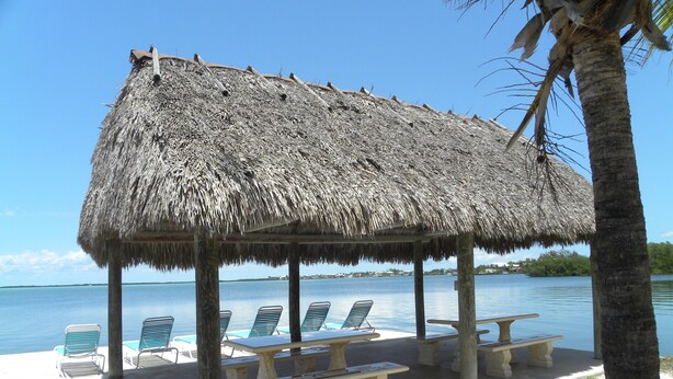 A beach hut with a thatched roof, surrounded by lounge chairs and a picnic table, overlooking a calm sea. - Rock Reef Resort (Key Largo)
