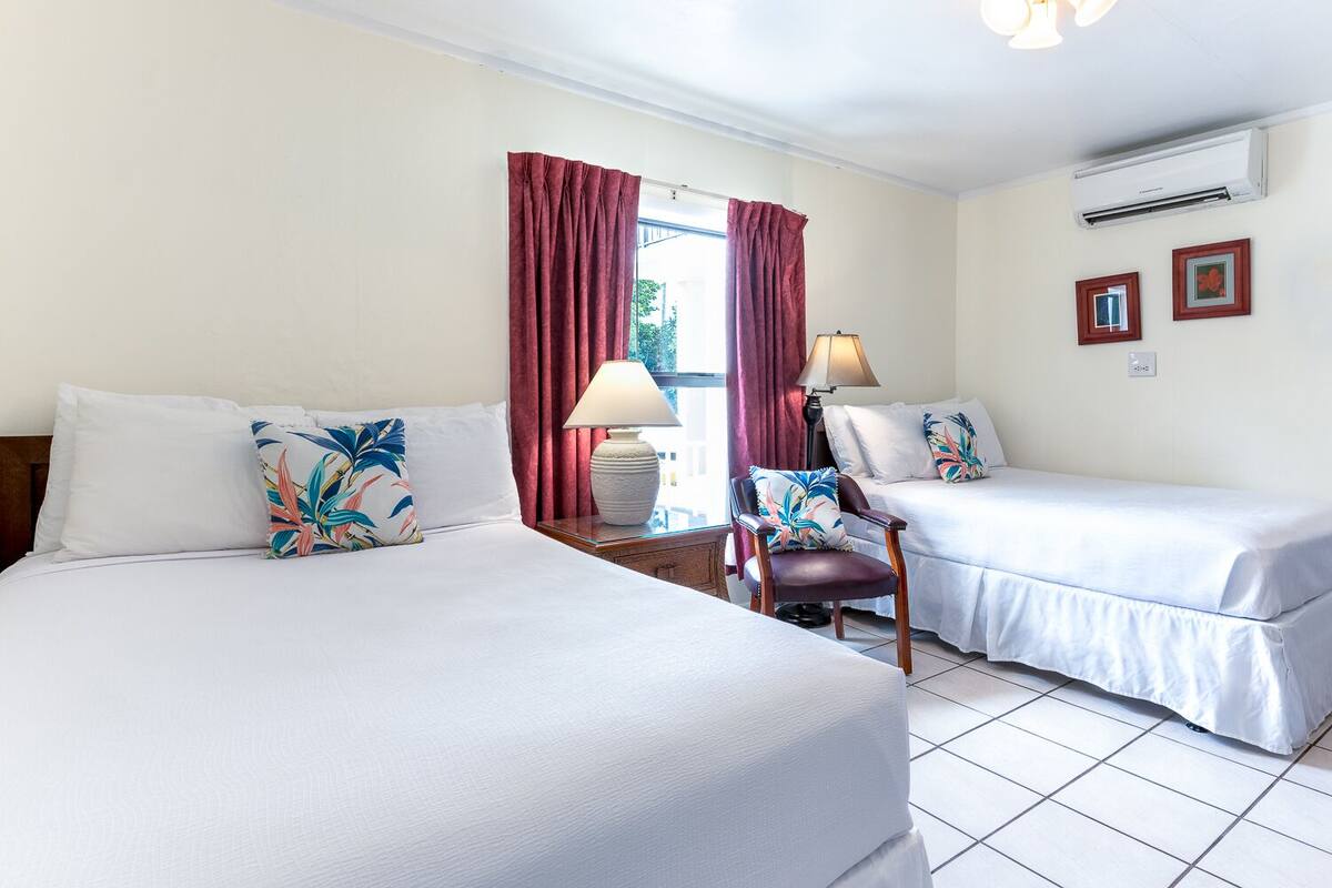 A hotel room with two beds, a chair, a lamp, and a window with curtains.