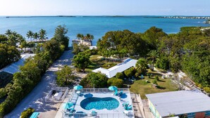 A pool area with a view of the ocean, surrounded by palm trees and a clear sky. - Rock Reef Resort (Key Largo)