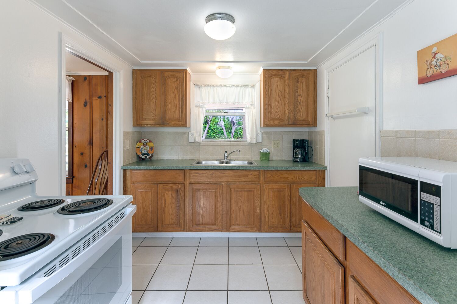 A compact kitchen with wooden cabinets, a white stove, a sink, and a microwave.