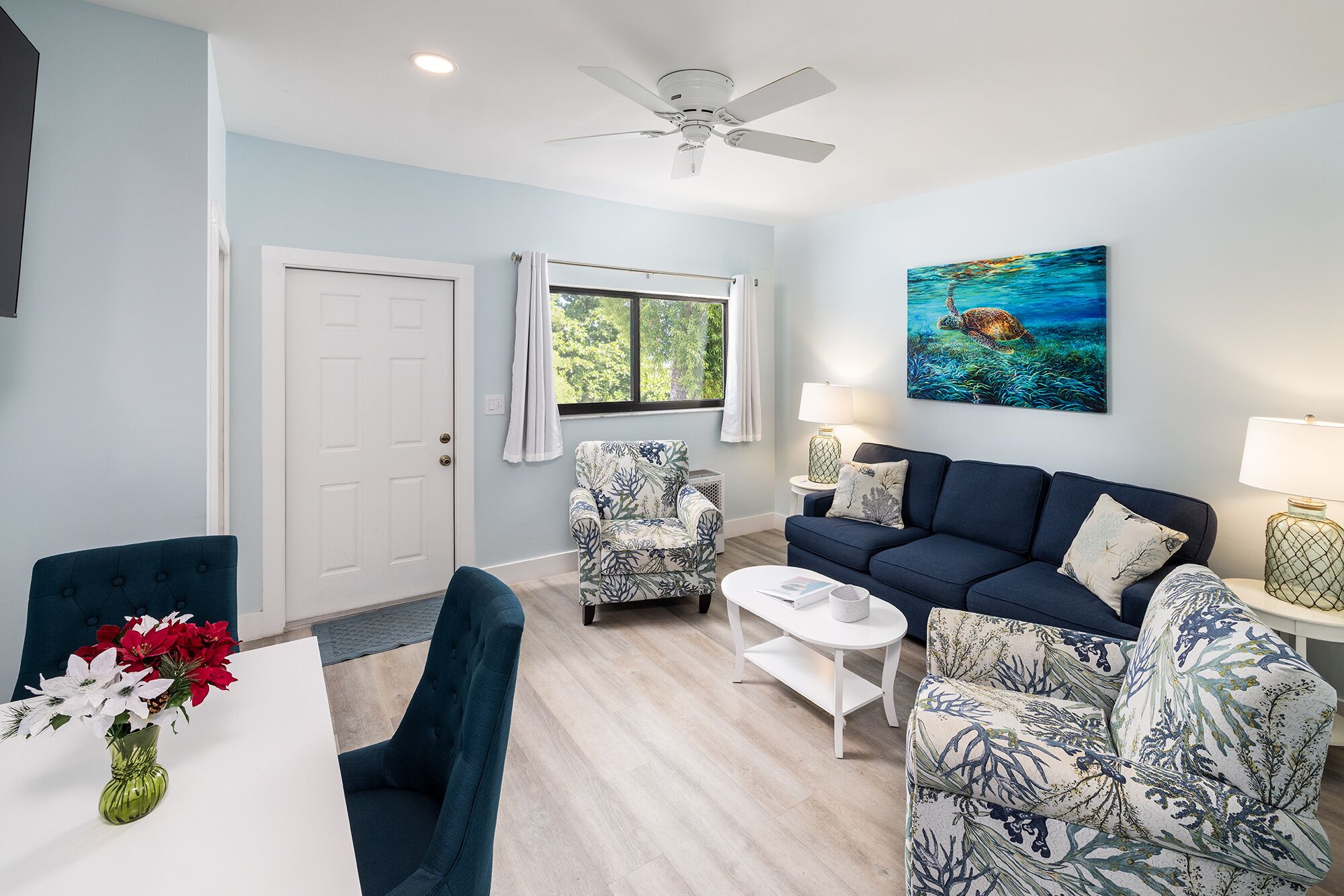 A living room with a blue sofa, patterned armchairs, a white coffee table, and a painting of a turtle on the wall.